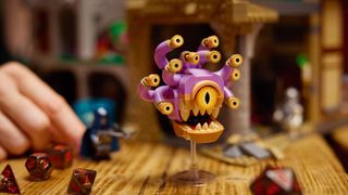 Lego Beholder on a table covered with dice, with a nearby hand holding a minifigure