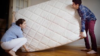 A couple moving a white mattress, with one carrying each end of the mattress