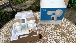 Ring Floodlight Cam Wired Plus carton and light on garden table before installing
