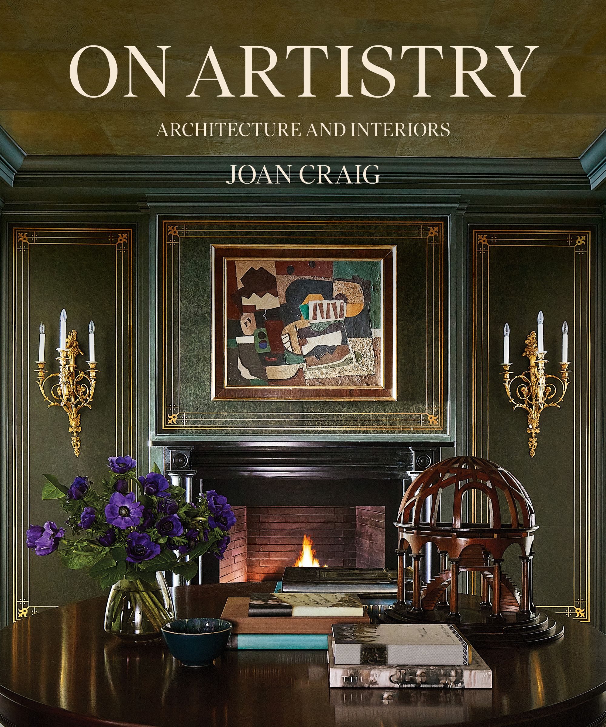 Joan Craig 'On Artistry' Front cover. Cozy entryway with dark green walls with gold trim, gold sconces on wall either side if a fireplace, round wood table in decorated with books and ornaments