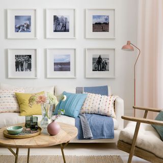 Photographs in square white frames arranged in a grid above a white sofa in a white living room