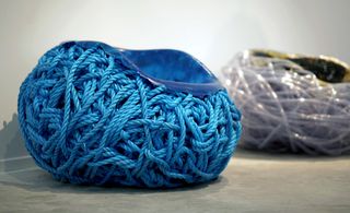 View of 'Meltdown' by Tom Price - a blue chair that resembles a ball of yarn and another chair in the background featuring a PVC hose design