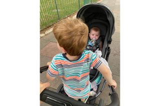 A photograph of our tester's son, taken from behind, as he stands on the ride-on board and his baby sister sits in the pram