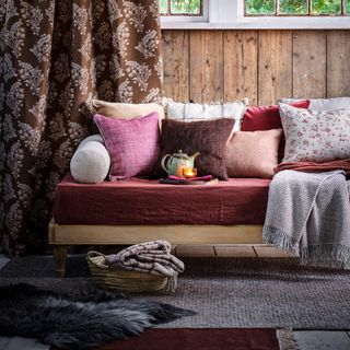 A brown living room with a sofa dressed with colourful cushions on a grey rug next to brown curtains
