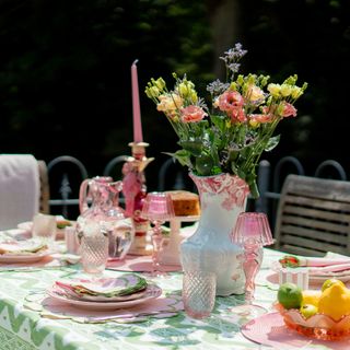 Anouska Lancaster's tablescaping with pink plates, glasses, table decoration and flowers in vase in outdoor dining area in garden