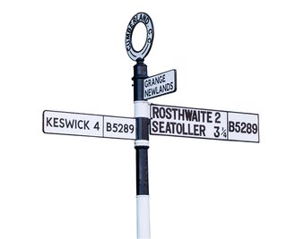 Old cast iron road sign at Grange near Keswick, Cumbria, England, UK isolated on white background.