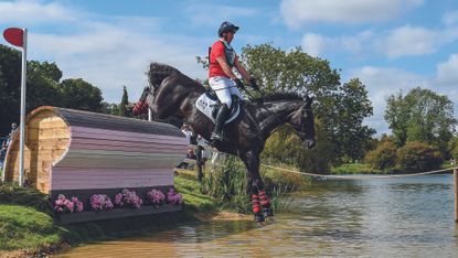 David Doel, a rider in a red top, and Galileo Nieuwmoed, a dark bay horse, jump into the water at Burghley 2023