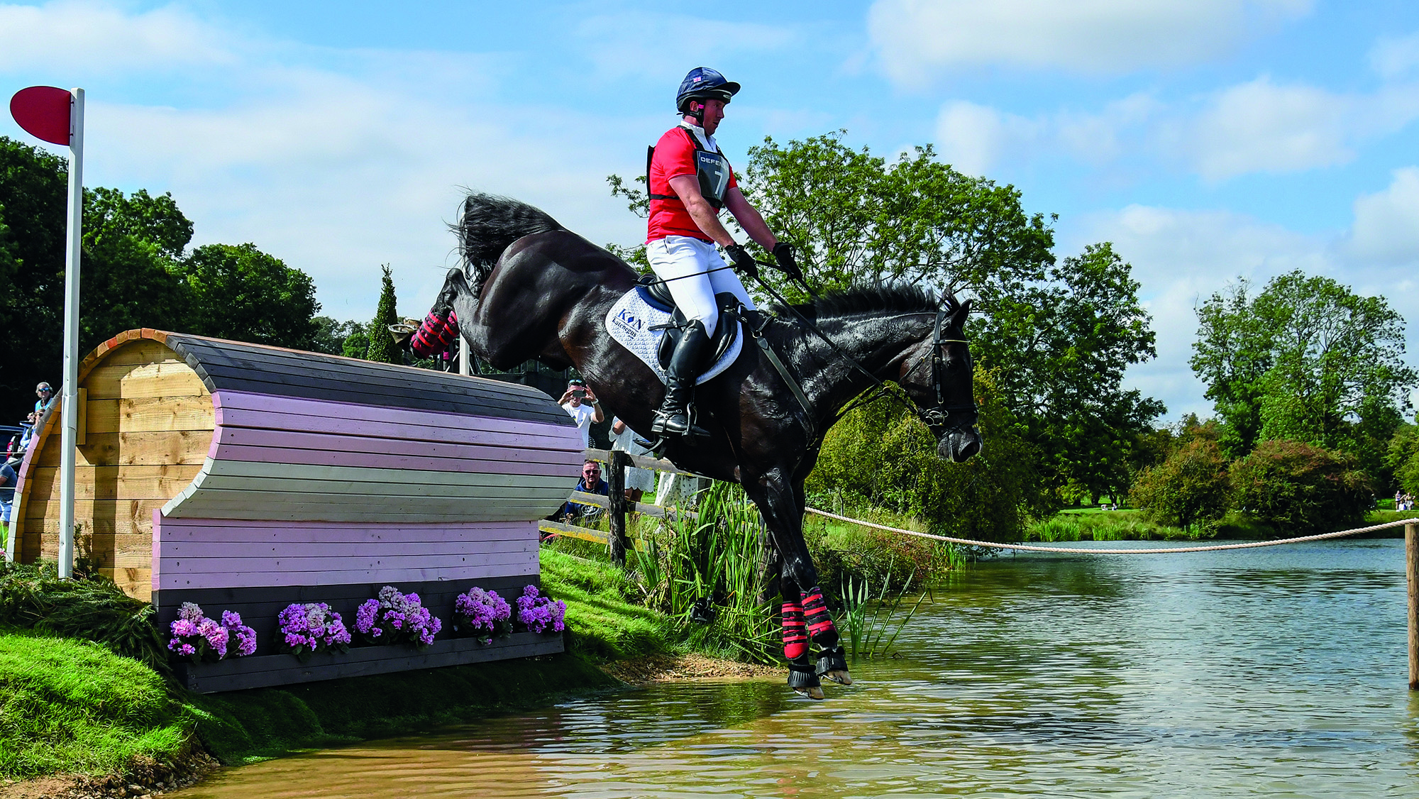 David Doel, a rider in a red top, and Galileo Nieuwmoed, a dark bay horse, jump into the water at Burghley 2023