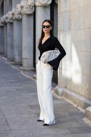 Irina Loginova wears black heels shoes ysl, white pants Massimo Dutti, black shirt with wide sleeves Avora studio, grey bag Bottega Venetta, sunglasses on November 16, 2024 in Barcelona, Spain.