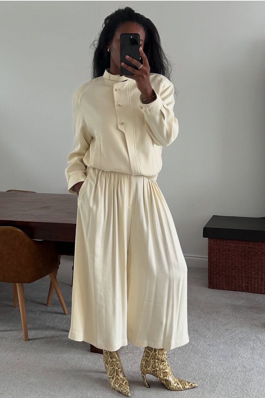 A woman wearing a cream color jacket, cream pants, and snake print boots