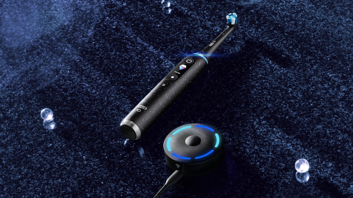 En svart Oral-B iO Series 10 eltandborste ligger på en mörkblå matta bredvid sin tillhörande laddningsplatta.