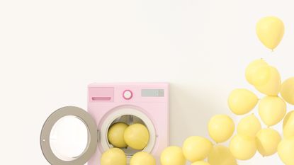 Yellow balloons floating out of a pink washing machine placed against a white wall.