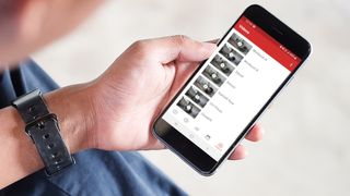 En person holder en mobil med StrongLifts app'en åben, der viser et galleri af fitness-videoer