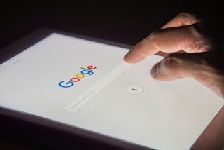 A hand using the Google search bar on a tablet computer