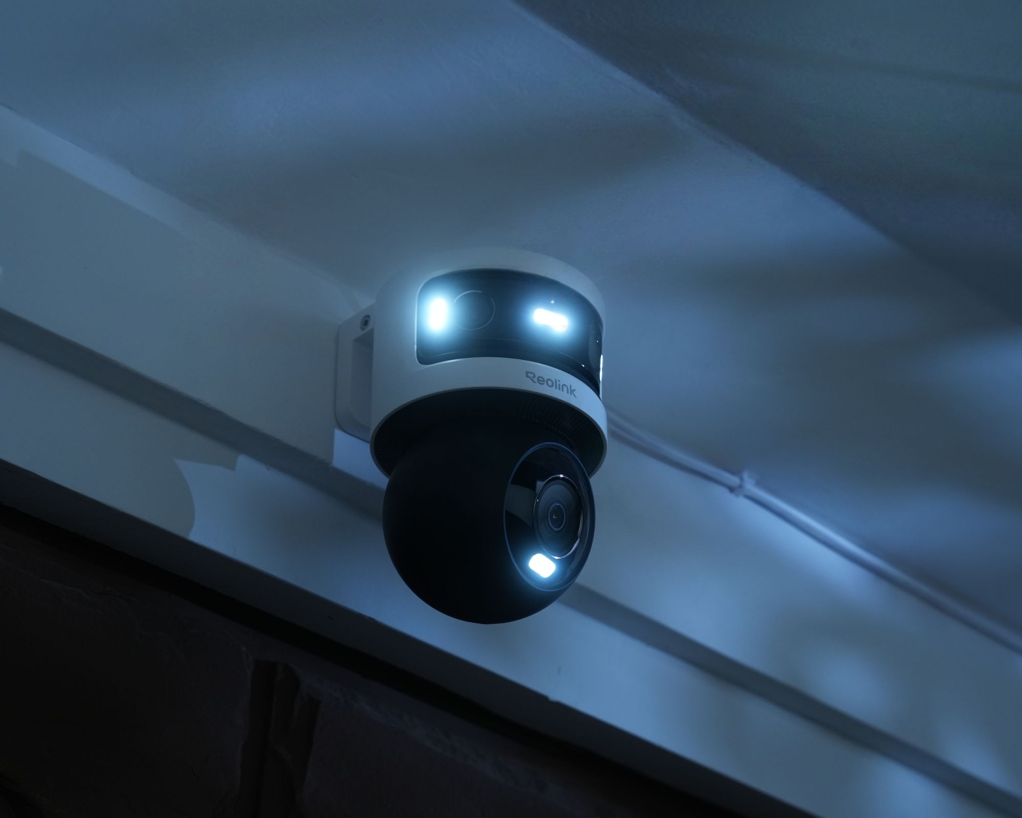 Reolink OMVI 3i PoE shown mounted on a white wall at night
