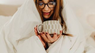 Woman wrapped up in a duvet holding a mug