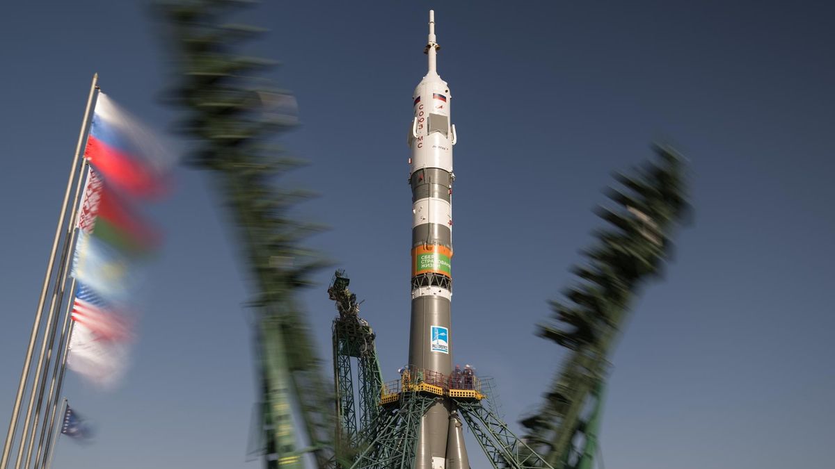 a brown-and-white rocket stands upright on a launch pad as two metallic skeletal structures fall away from it