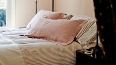 A peach bedroom with striped pink bedding, pink pillows, and a dark brown and white polka dot curtain in the foreground.