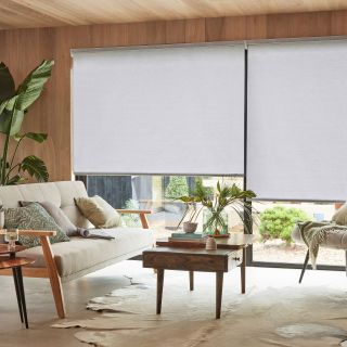a neutral living room covered in timber panelling and large sliding doors covered in neutral roller blinds