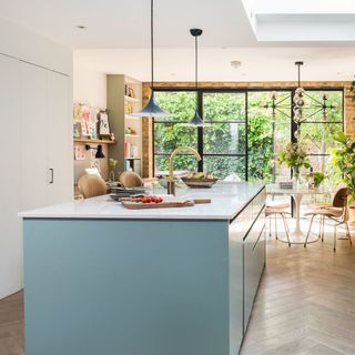 Open plan kitchen dining area with pale blue glossy island and pendant lighting