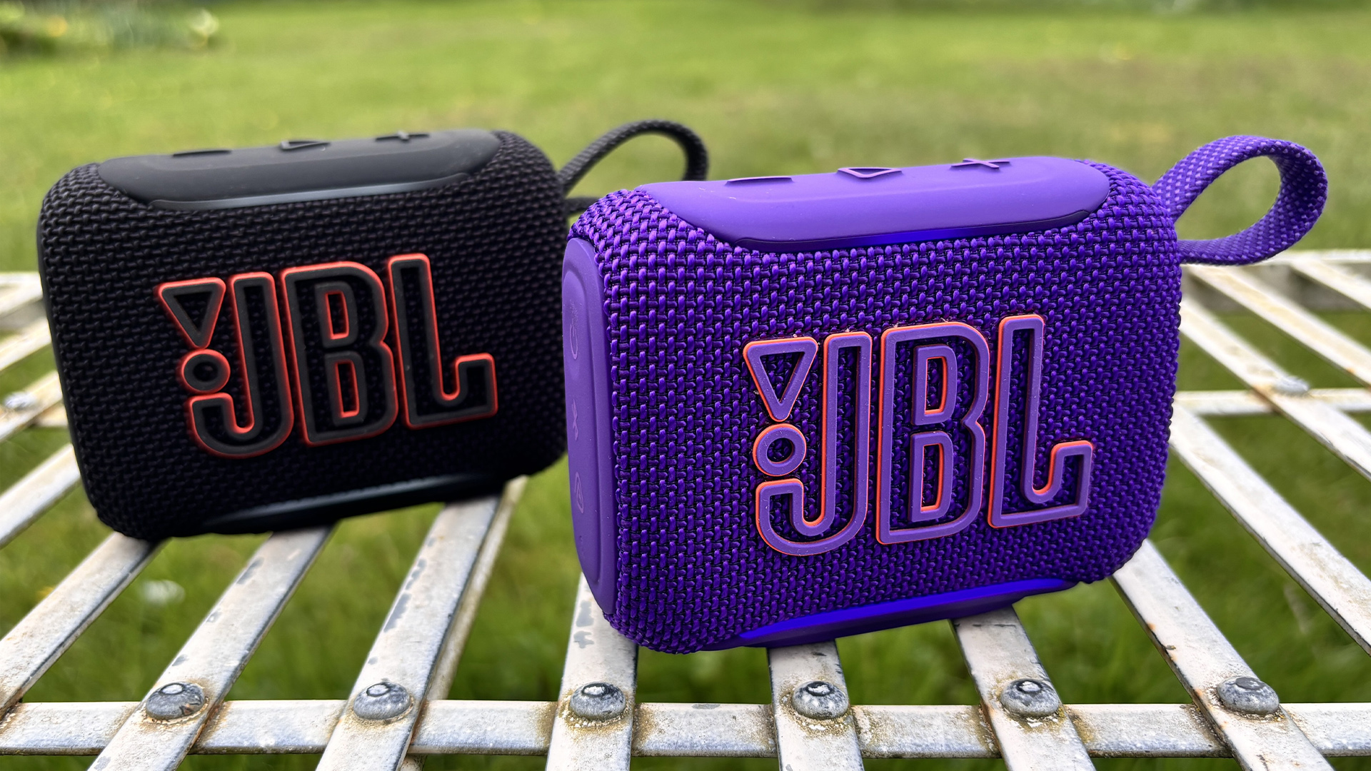 Two JBL Go 5 speakers, one in purple finish in front of the one in black finish