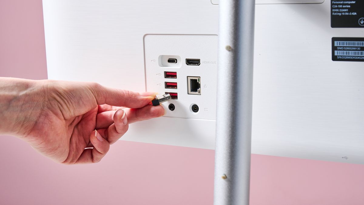 Close-up of ports on Acer Aspire C24, with hand inserting a USB dongle, against a pink background
