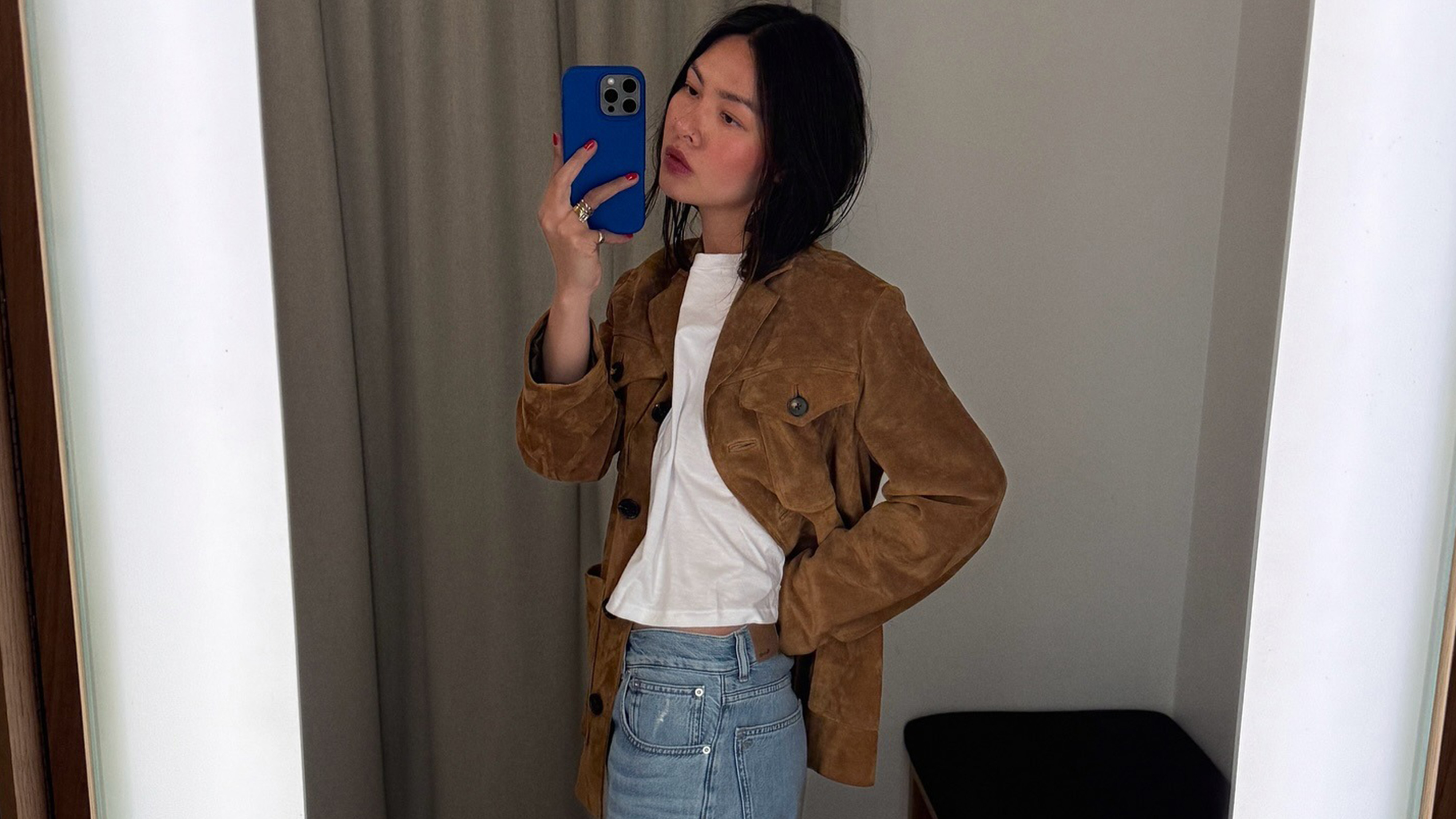 Mimi wears a suede jacket, white tee, and blue jeans.