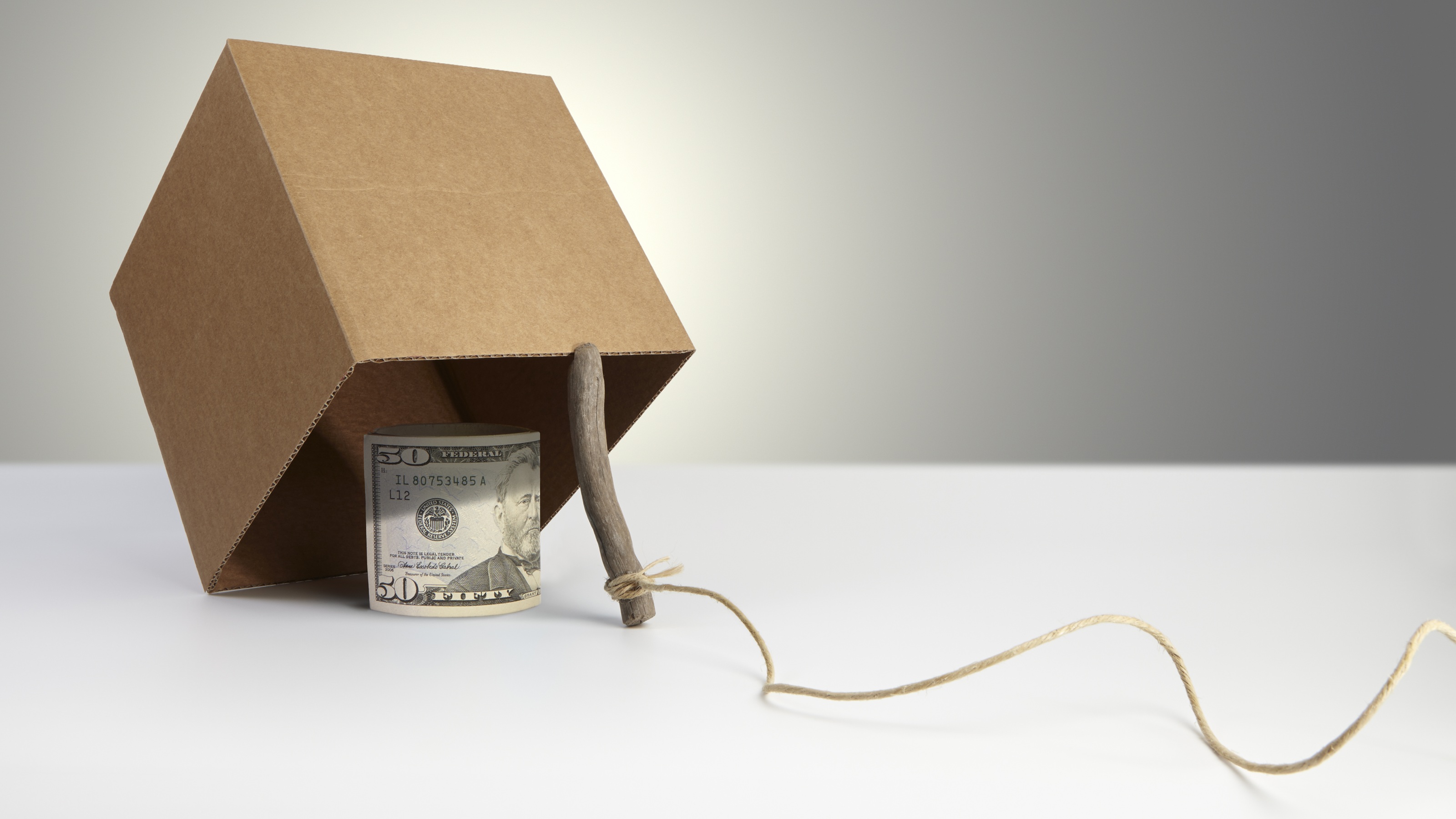 A 50-dollar bill sits under a tilted box that's been rigged as a trap.