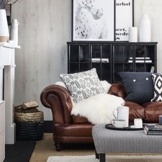 A grey living room with a tan leather sofa with sheepskin rug and grey footstool coffee table
