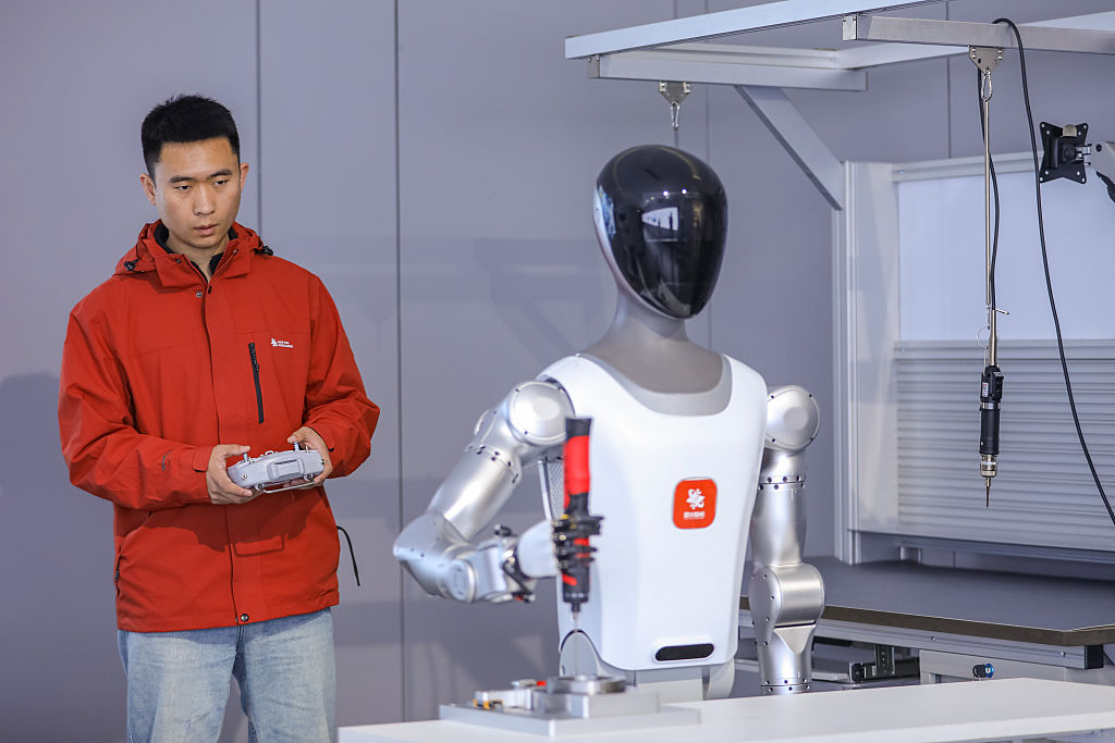 A technician debugs a humanoid robot at a factory