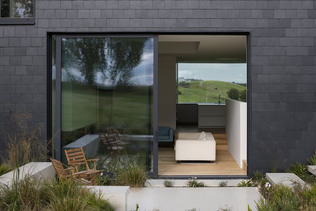 A black tiled house with open bifold doors leading into a lounge with a large picture window in the background with green fields