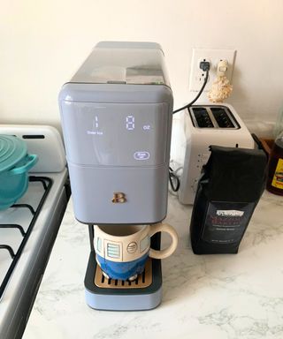 The new Drew Barrymore single serve coffee maker in blue being used in a white kitchen