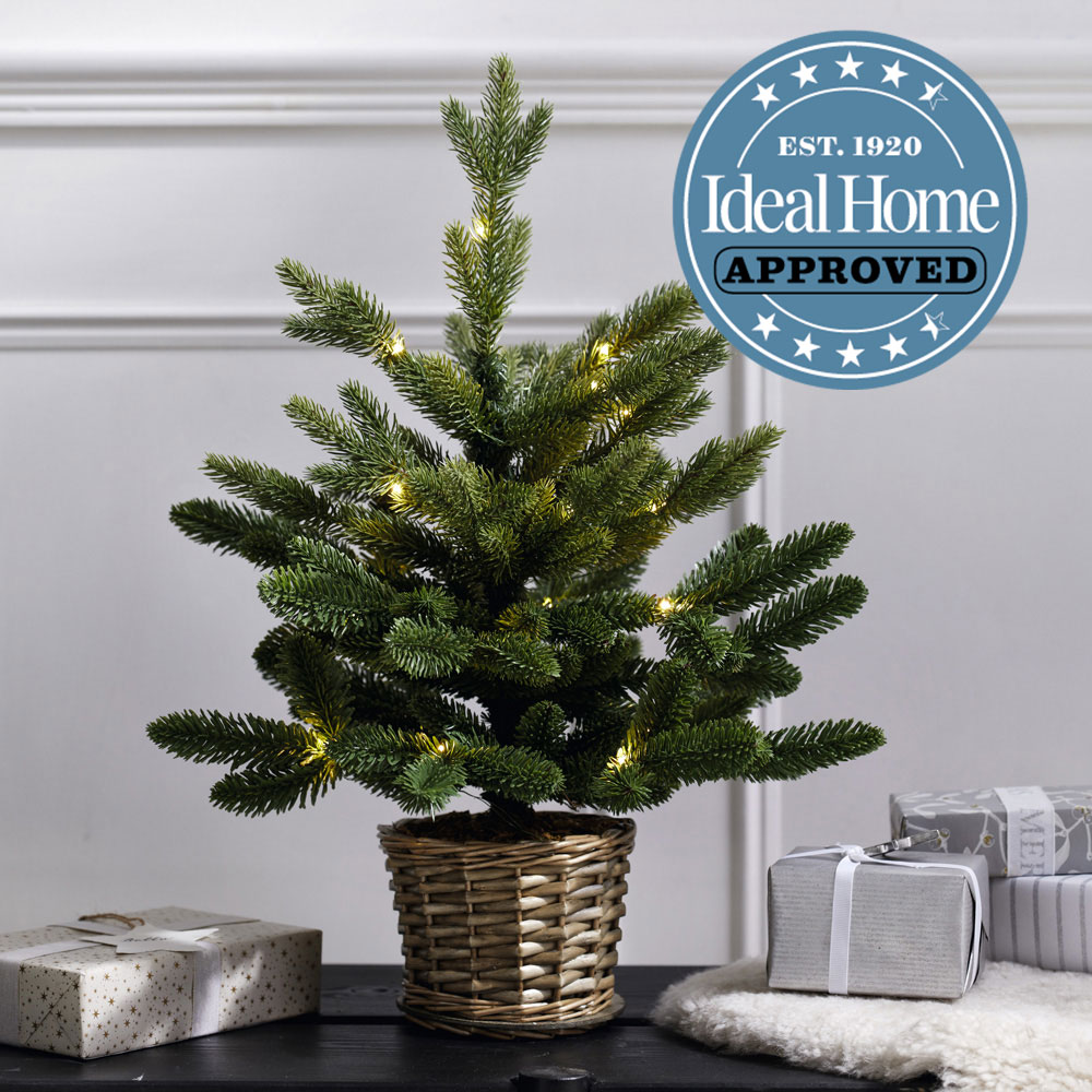 A small potted Christmas tree on a table surrounded by gifts with the Ideal Home approved logo.