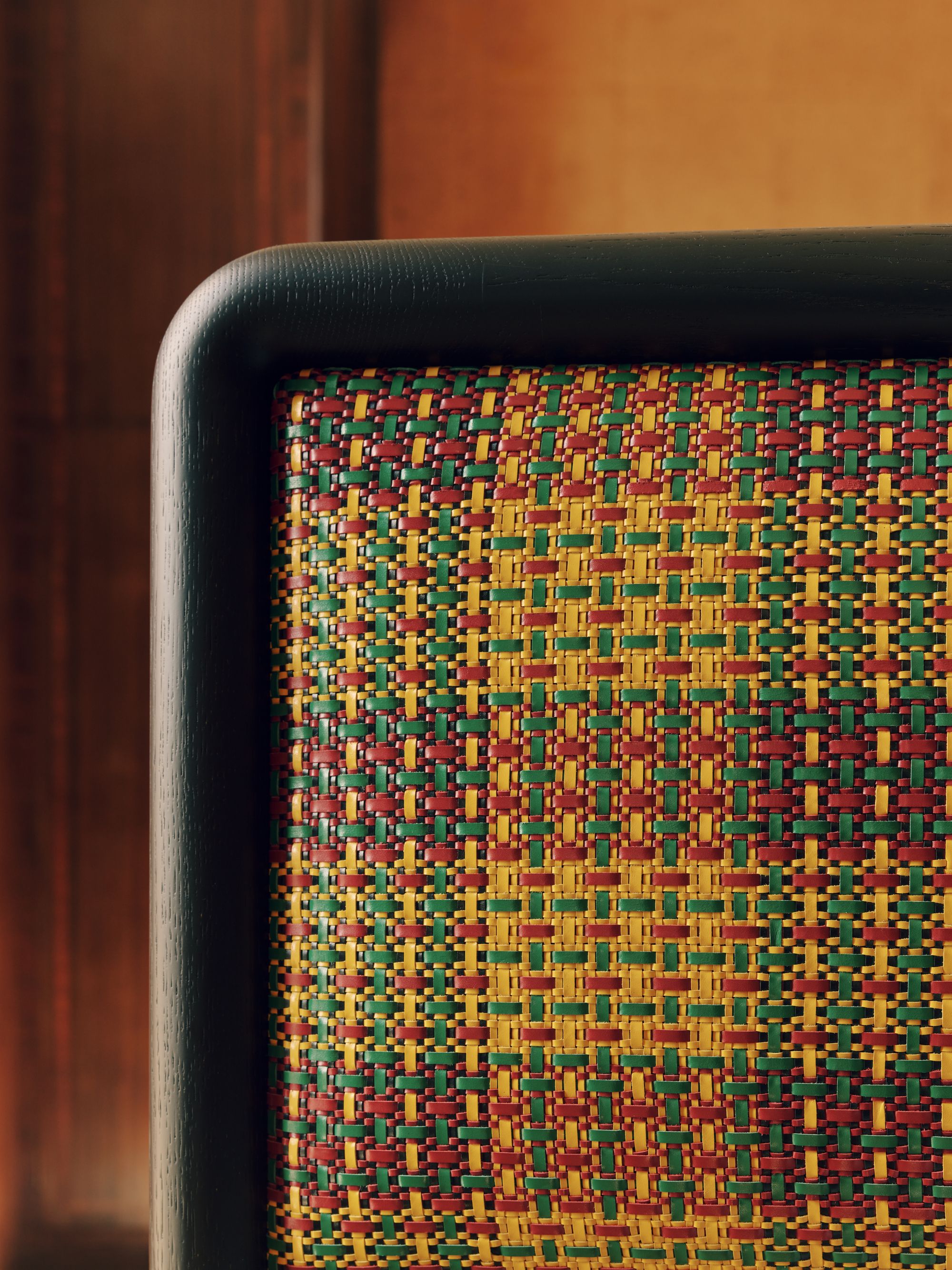 Close-up of a headboard that has a leather edge and a yellow, green, and red woven plaid fabric.