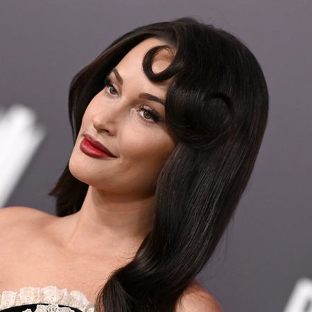 a white woman with dark hair poses in front of a gray backdrop at a red carpet event