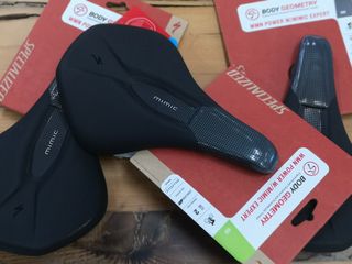 Specialized Power MIMIC women's saddle is shown top down in the image on it's carboard packaging. It is on top of other Specialized saddles, which are also in their packaging.