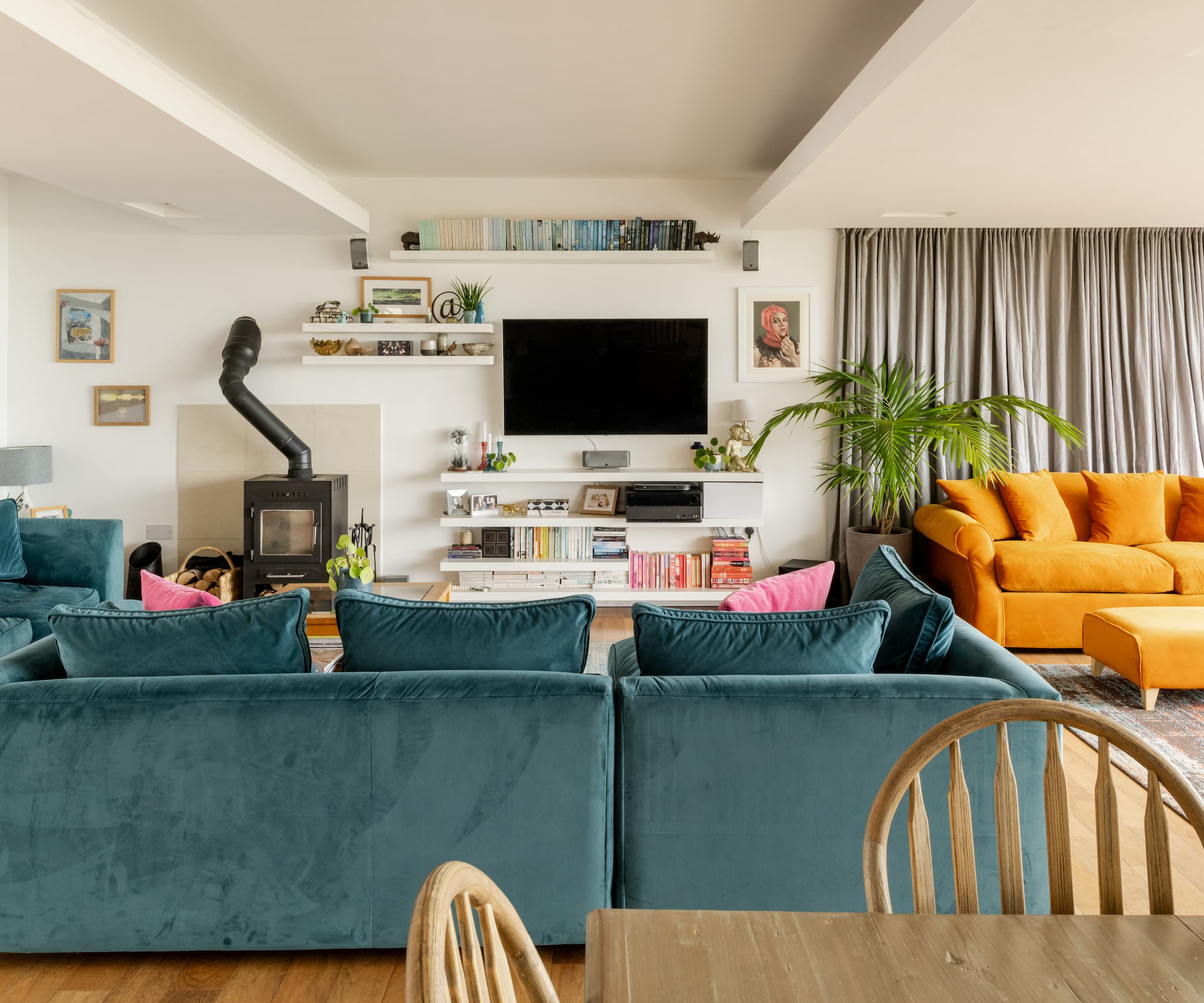 A living room with a woodburner and wall shelving units and an orange and blue sofa