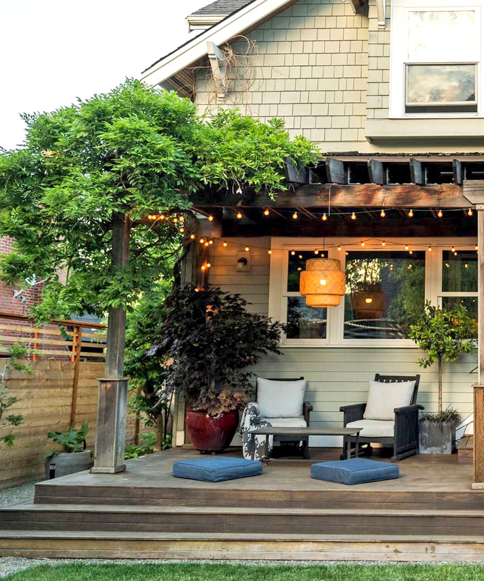 pergola on deck attached to wall of house with climbing plants, garden furniture, potted plants, and fence, lawn and house