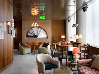 Interior view of the lounge at White City House featuring grey flooring, wood covered and dark beige walls, colourful wall art, a multi-sphere pendant light, round tables and seating in different colours