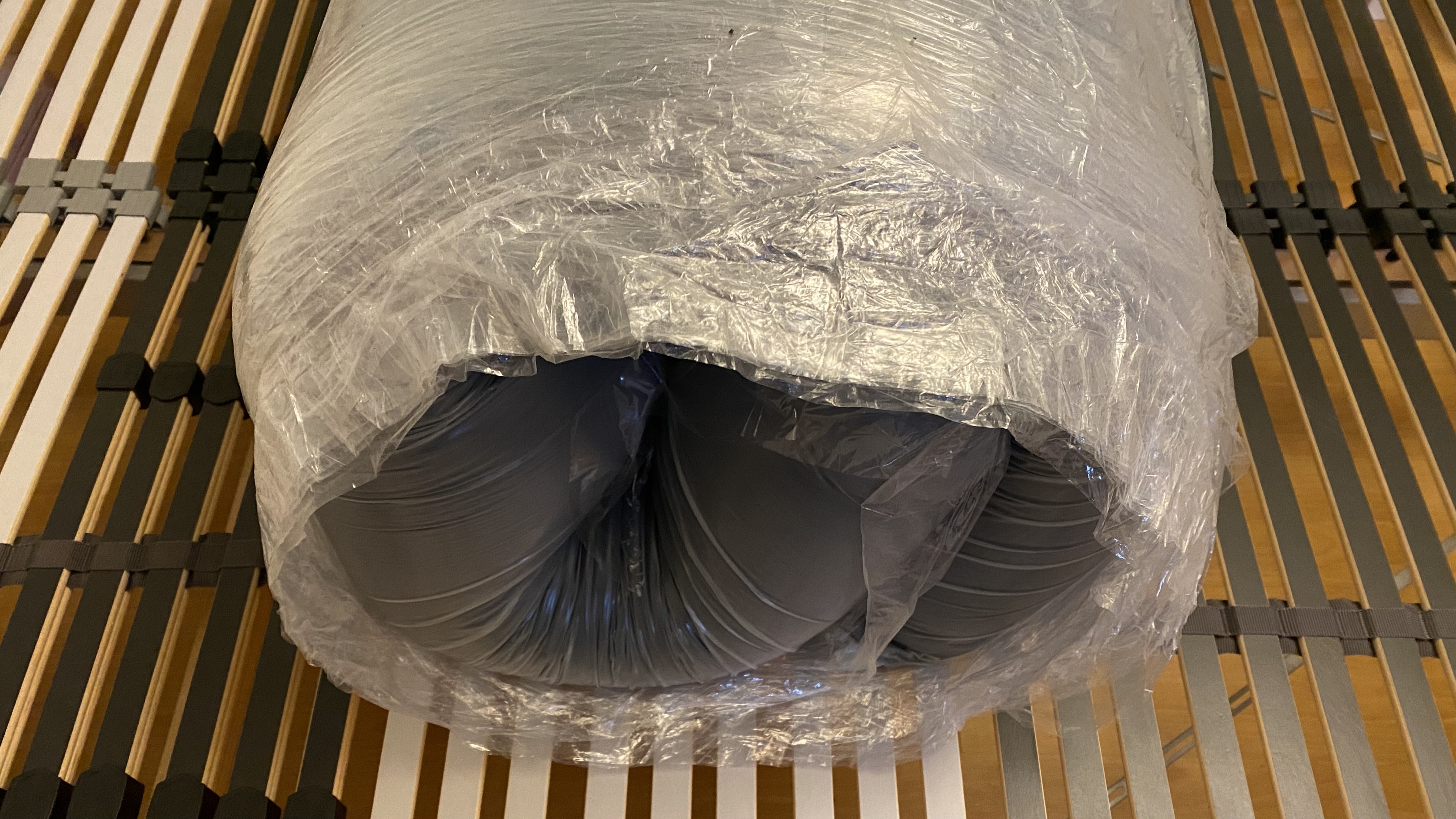 Zoma Mattress unboxed but wrapped in plastic on our tester's slatted bed frame.