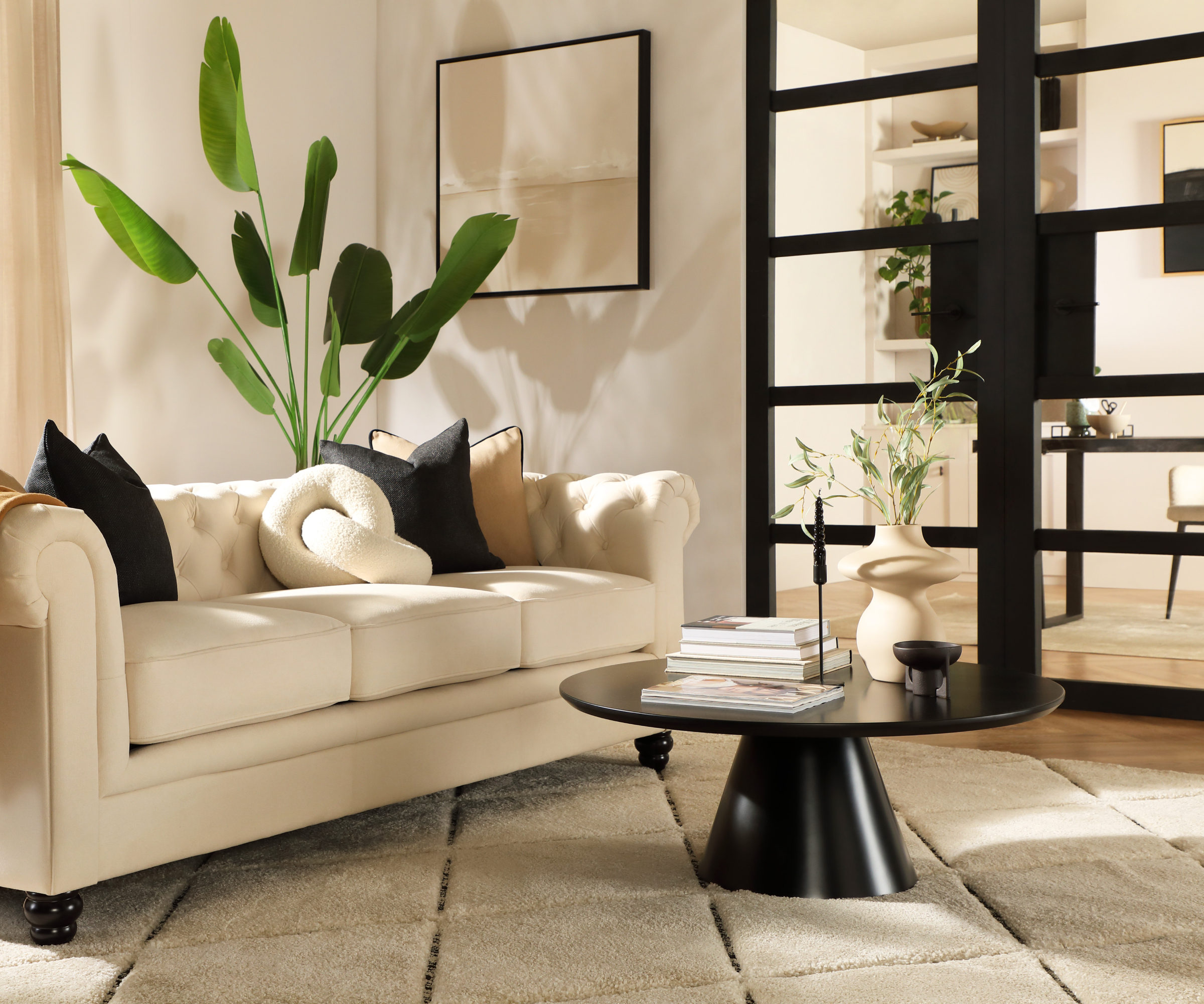 living room with cream sofa, black coffee table, plants and black framed glazed doors leading to another room