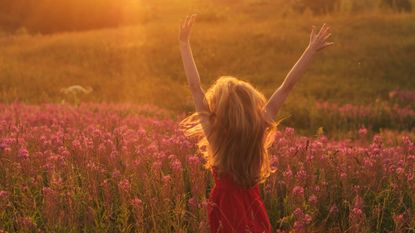 Woman dancing and jumping around in a field full of pink flowers 