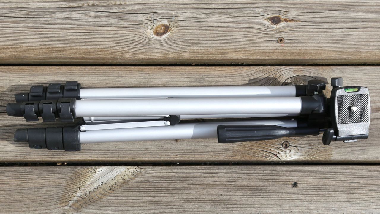 a silver tripod with black accents collapsed, and laying down on a wooden surface.