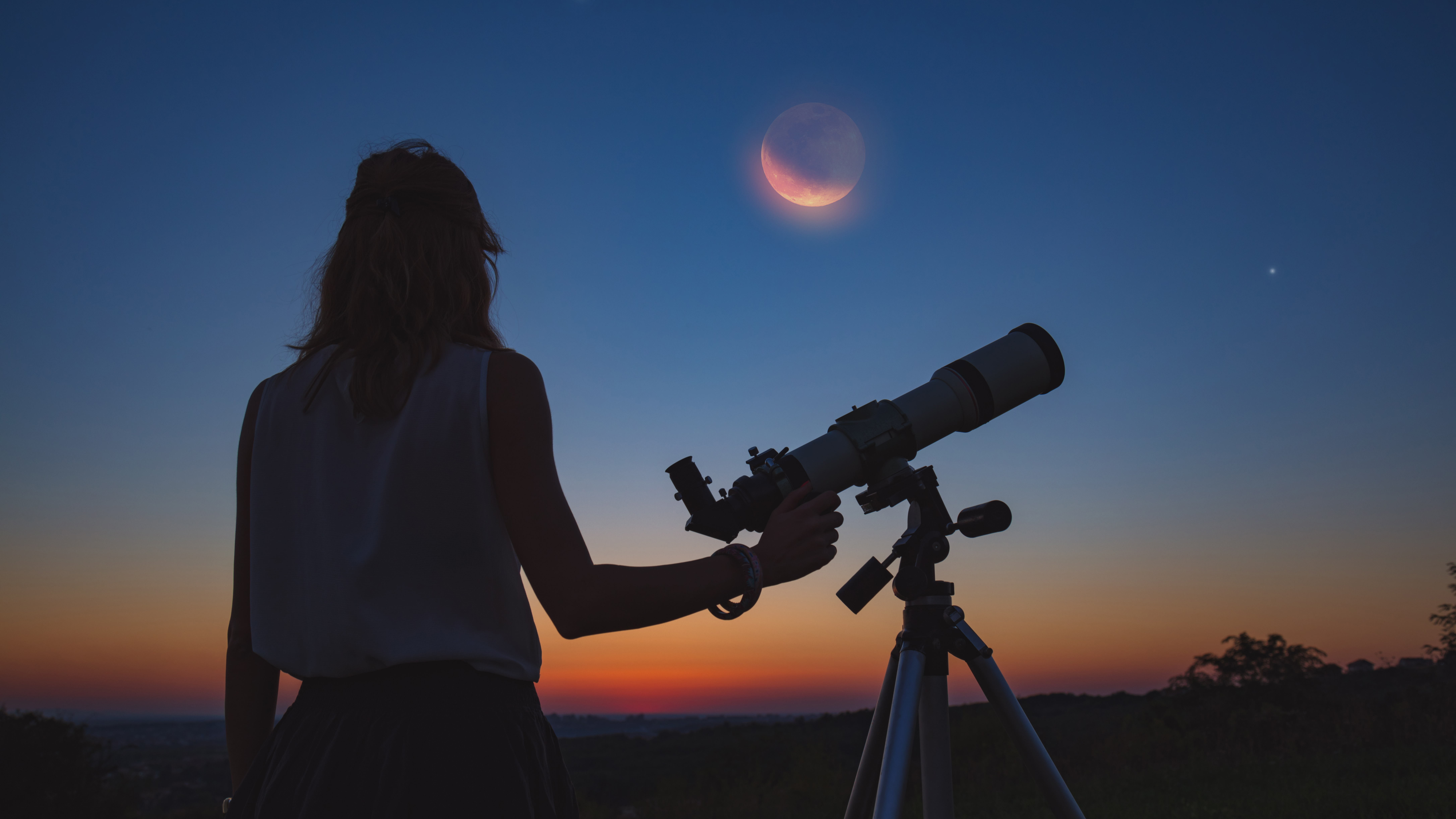 A woman standing next to a telescope looking up at the moon