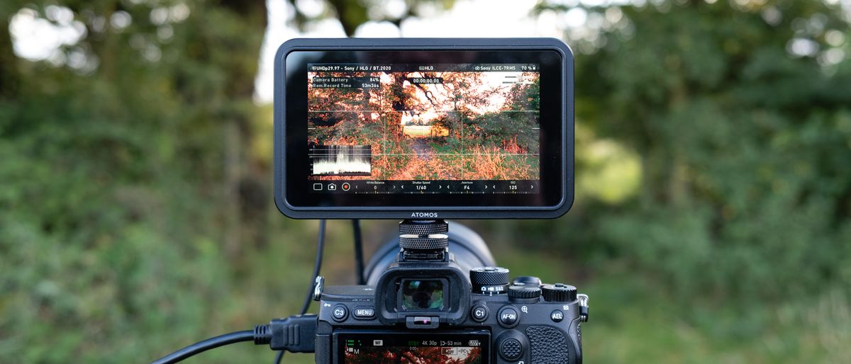 An Atomos Shinobi II camera monitor on top of a camera outside in a field