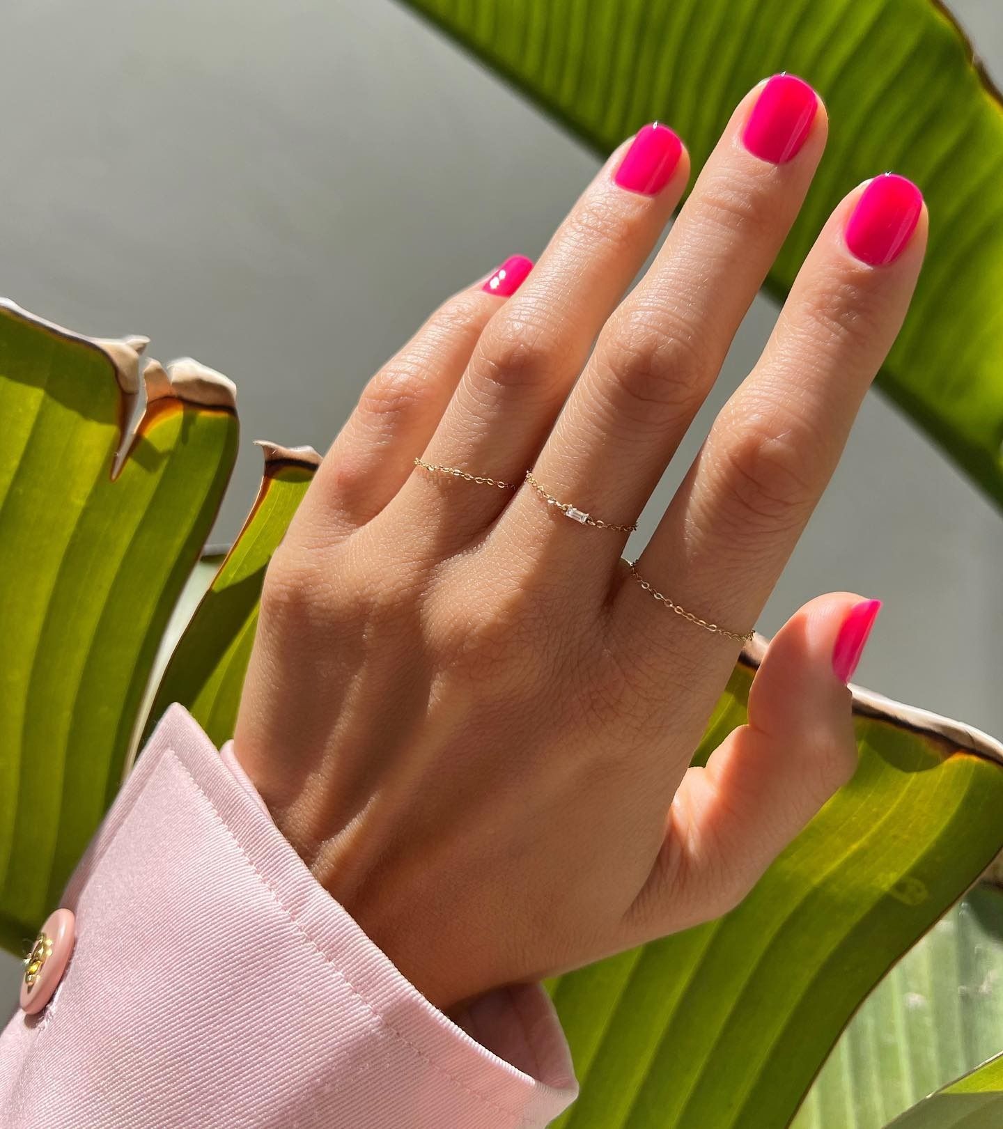 Bright pink nails with palm leaves in the background