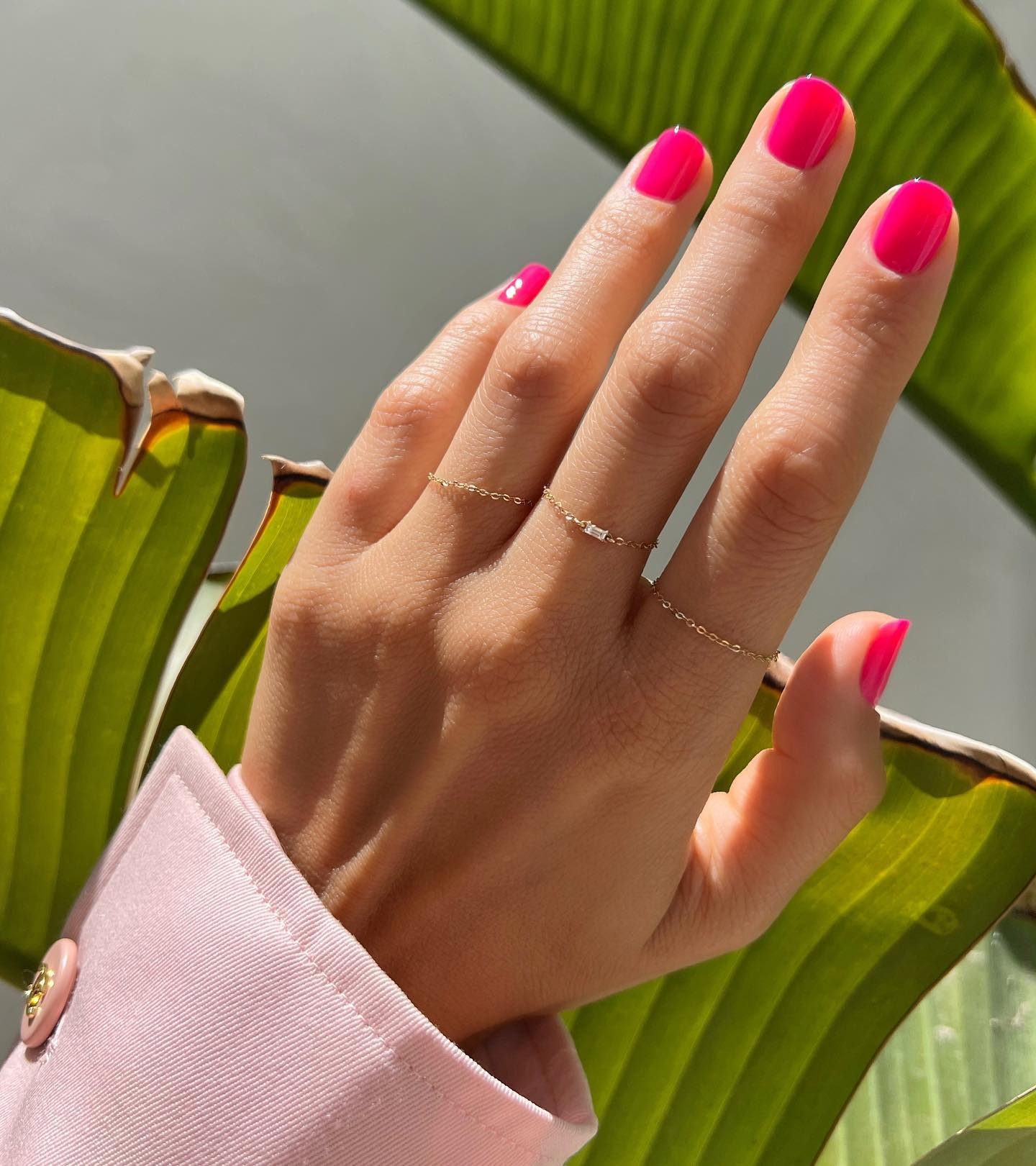 Bright pink nails with palm leaves in the background