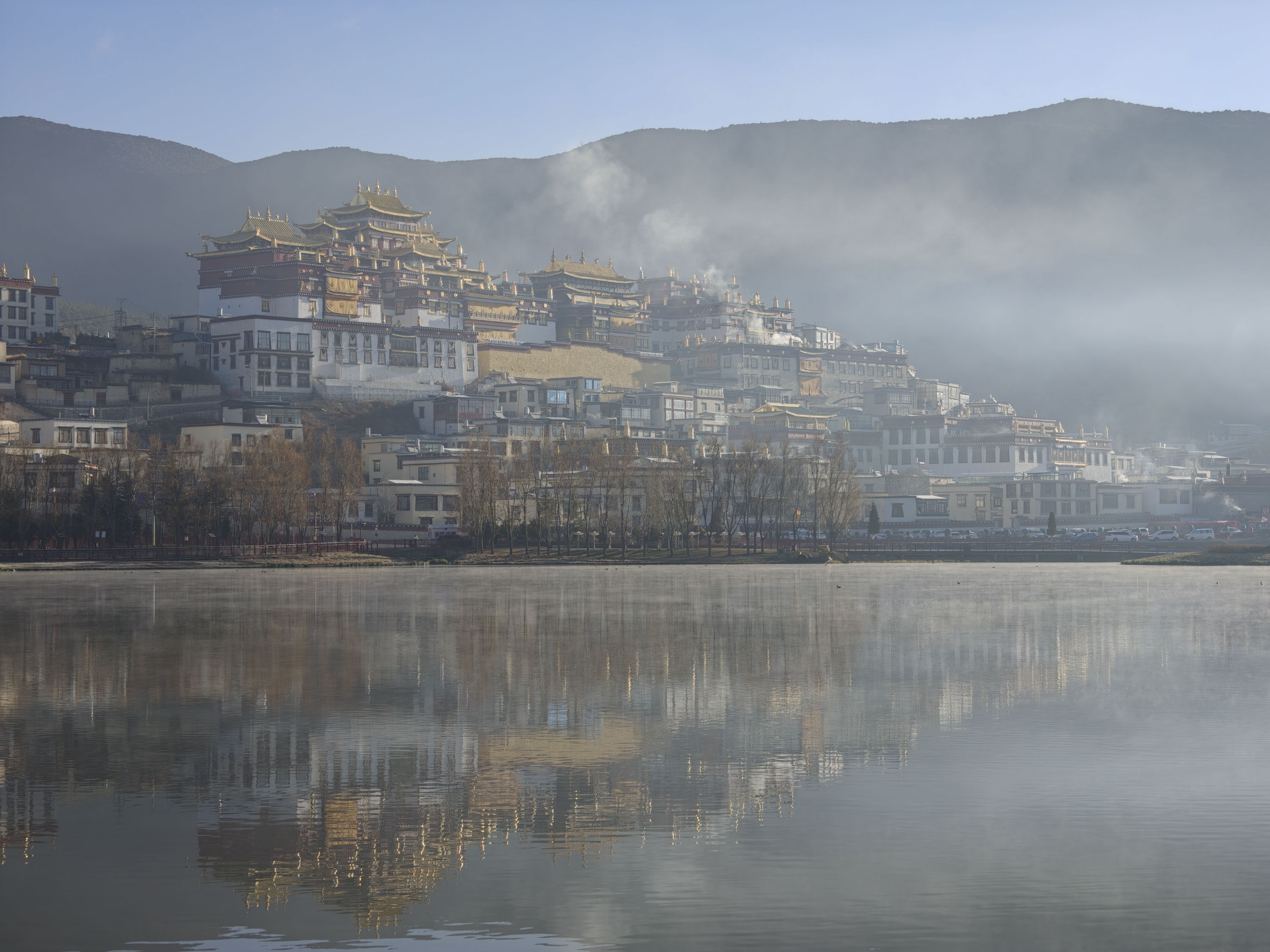 A buddhist monastery and town reflected in a still lake at first light, with a touch of mist