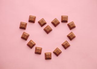 A light pink background with small chocolates in the shape of a heart.