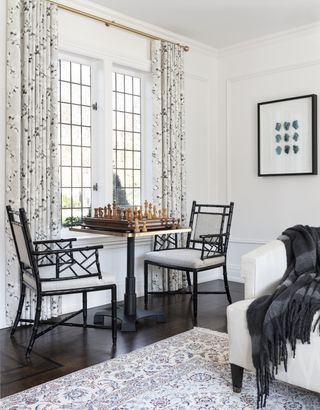 living room with chess table and two chairs, white couch, floral drapes, vintage rug, hardwood floor